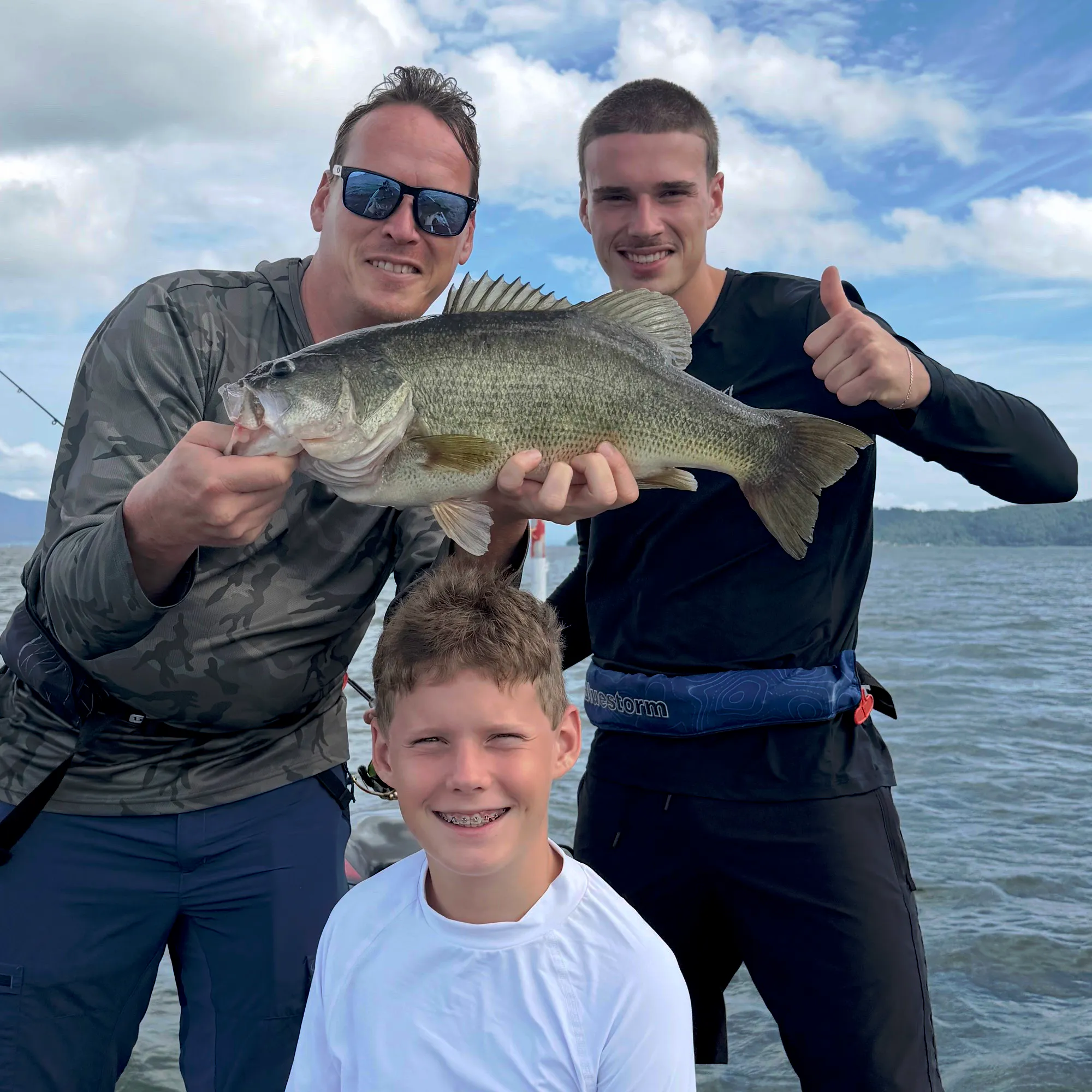 Three guests on a bass boat holding a largemouth bass together on Lake Biwa