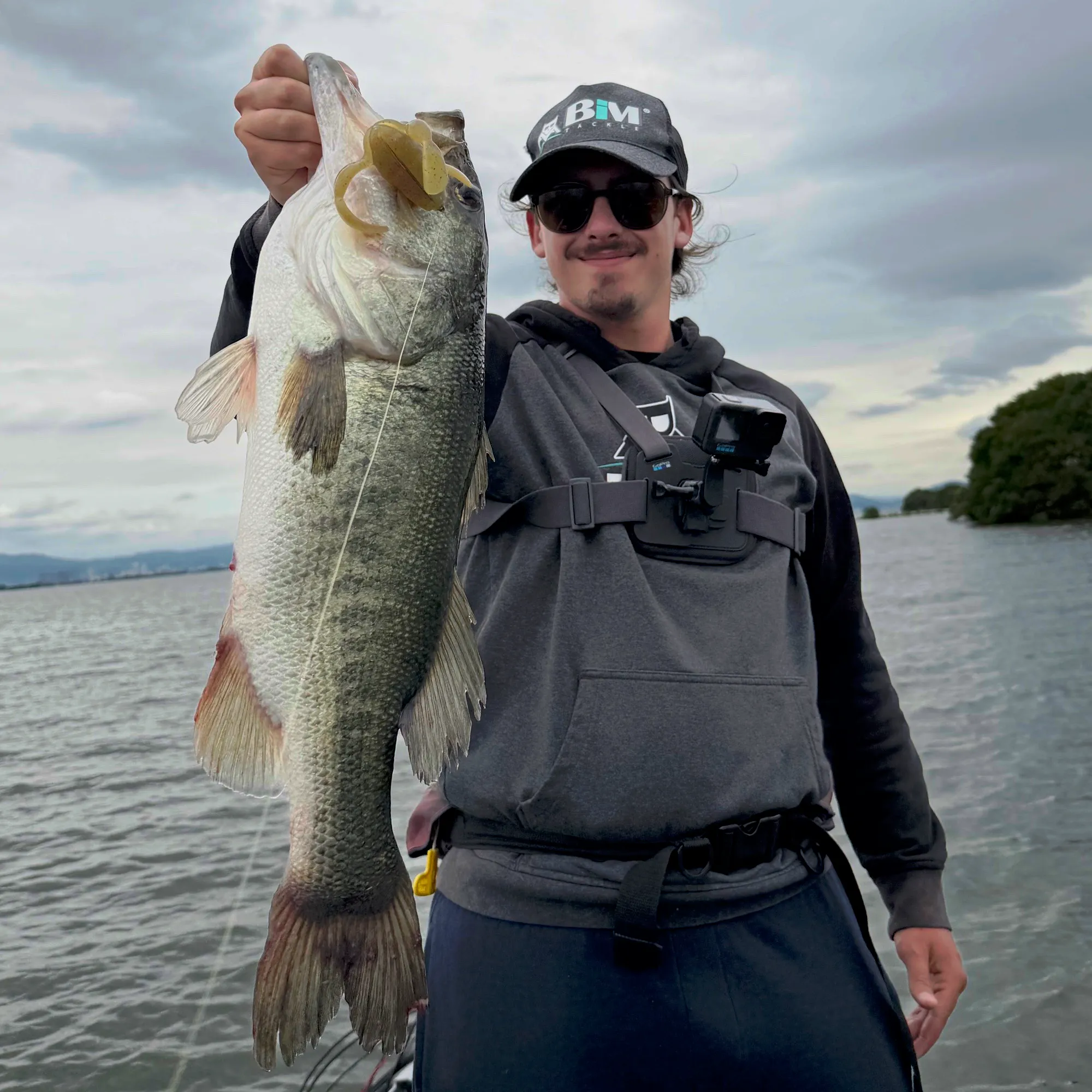 A guest holding a largemouth bass with a soft plastic lure in its jaw on Lake Biwa