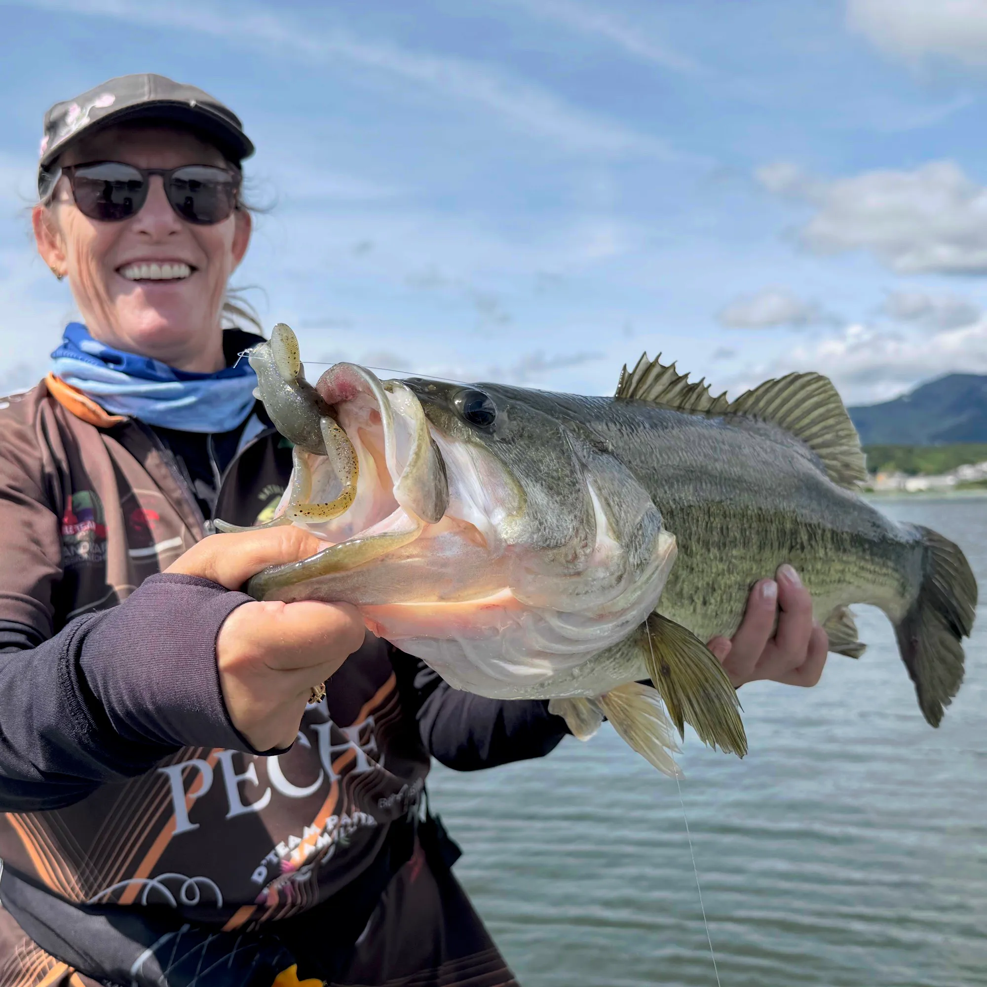 A smiling guest holding a largemouth bass caught on a soft plastic lure on Lake Biwa
