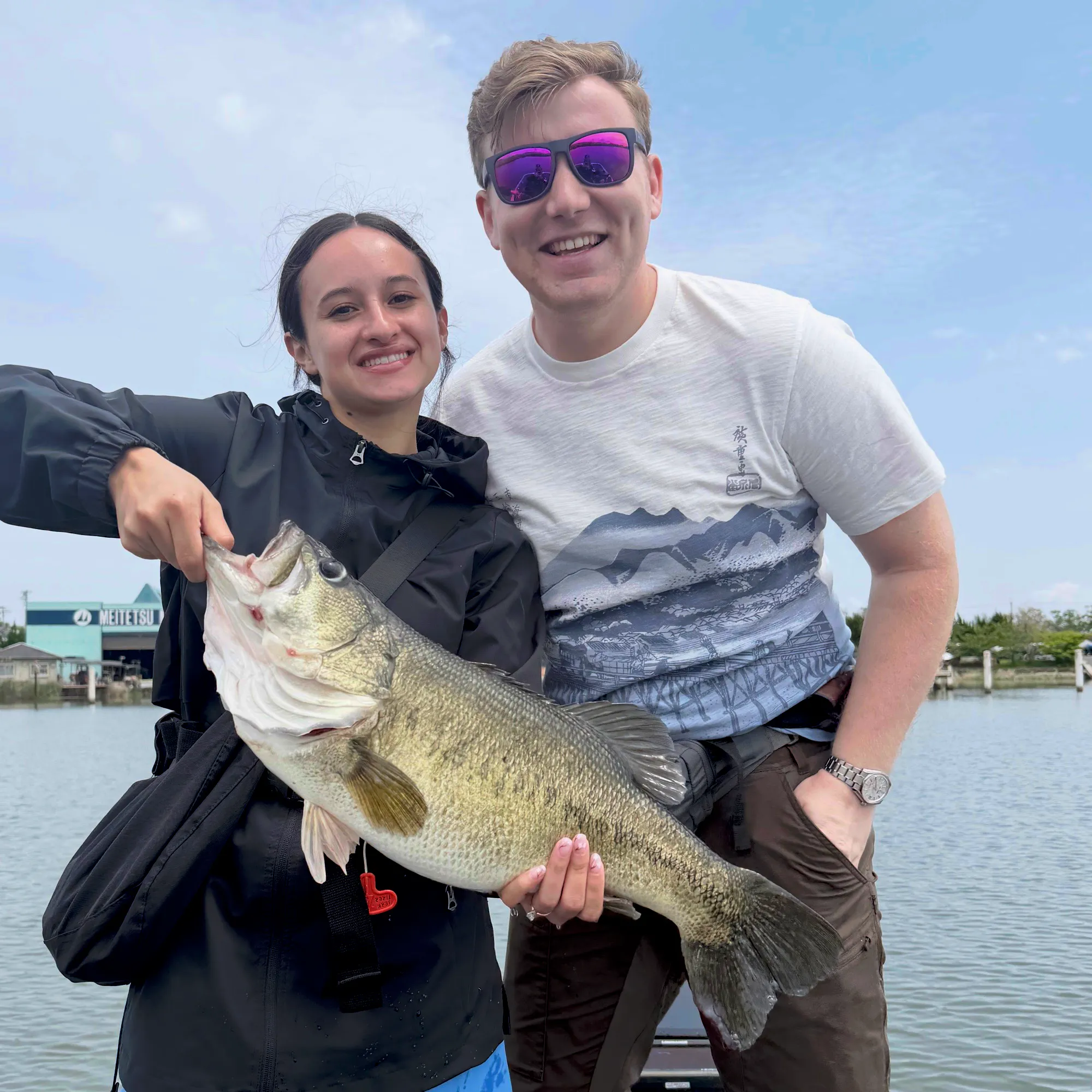 Two guests holding a largemouth bass together beside the water
