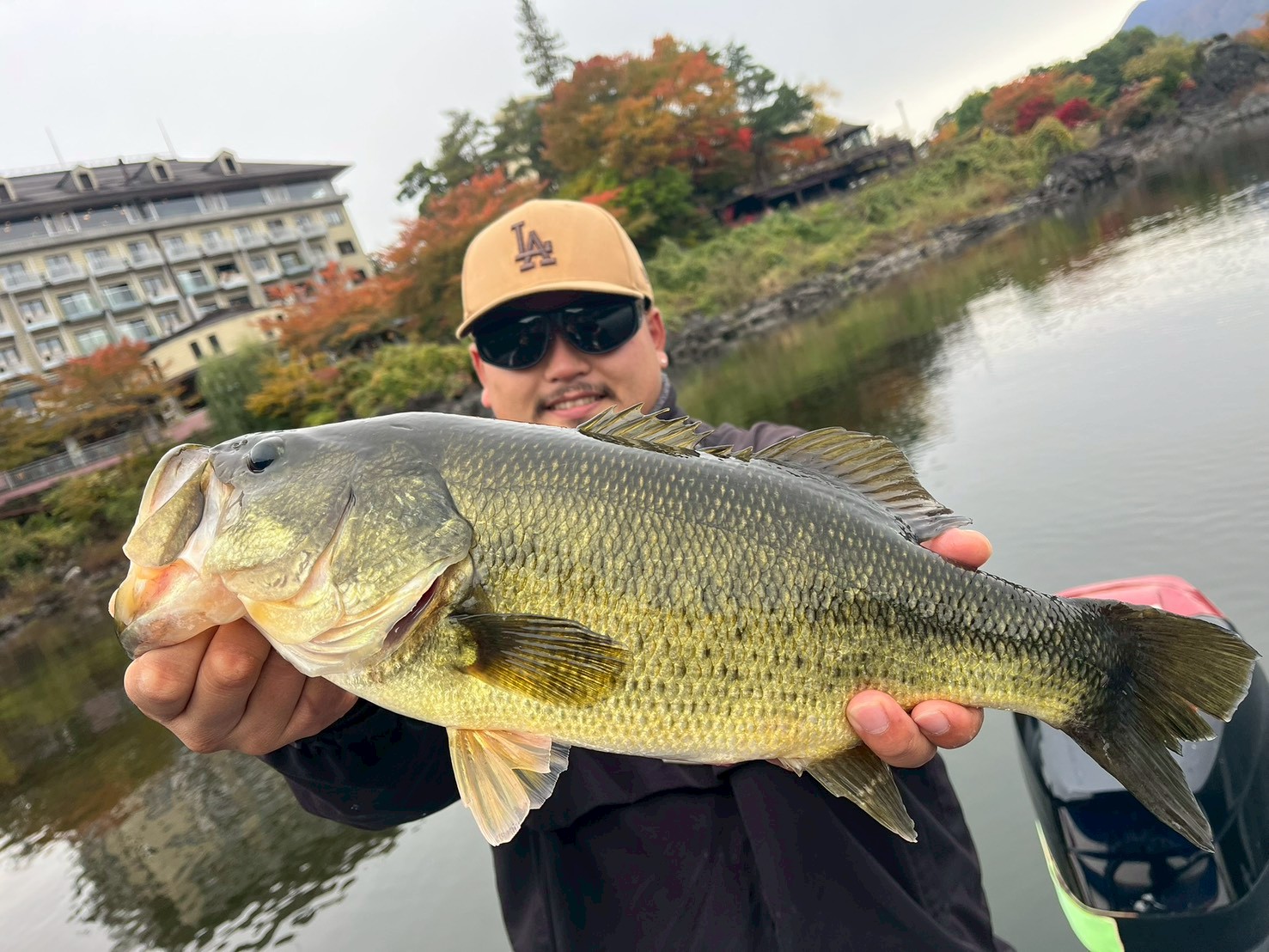 Angler holding a large largemouth bass on Lake Kawaguchi with autumn foliage behind