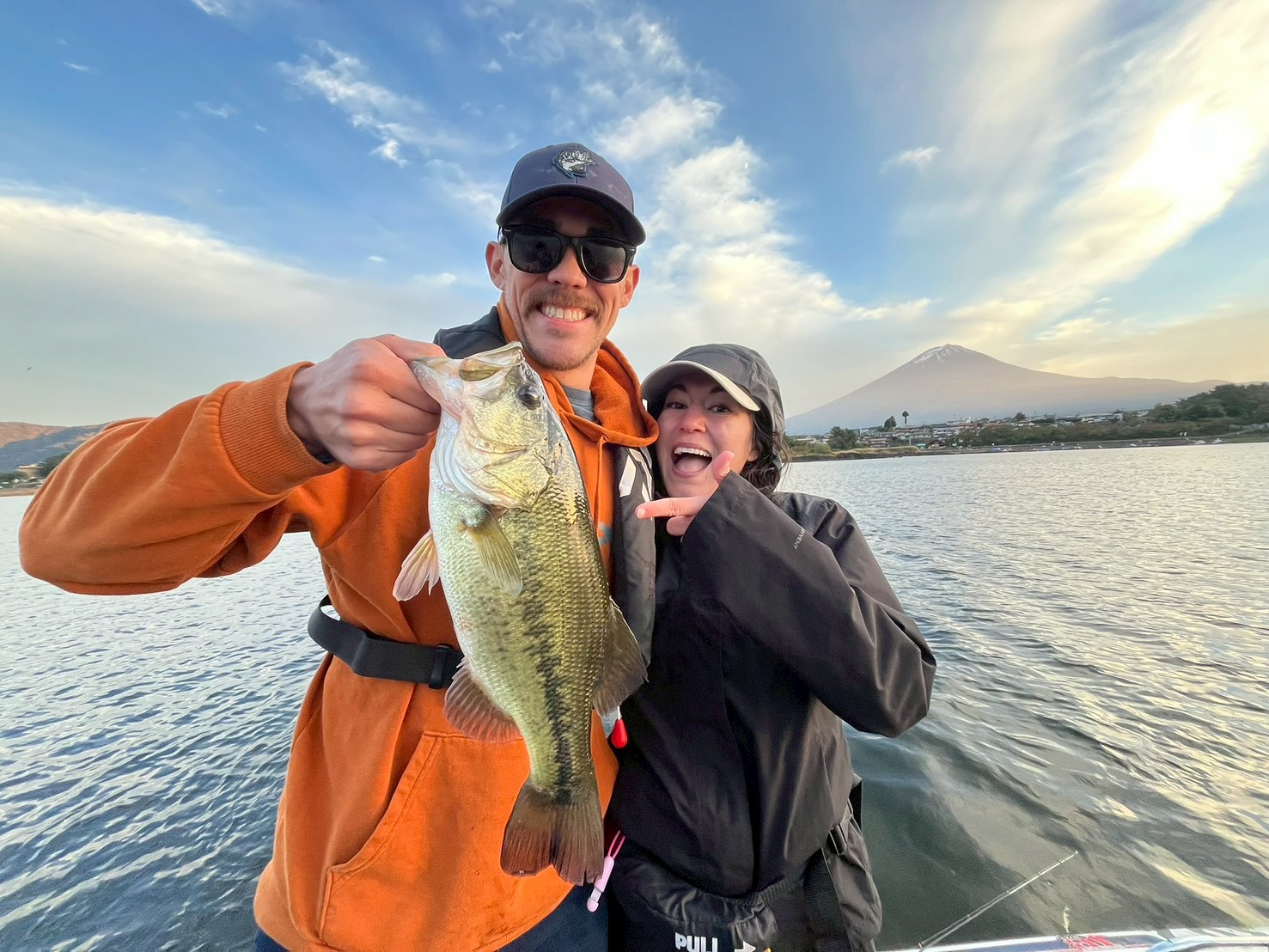 Two guests celebrating a largemouth bass on Lake Kawaguchi with Mt. Fuji at sunset